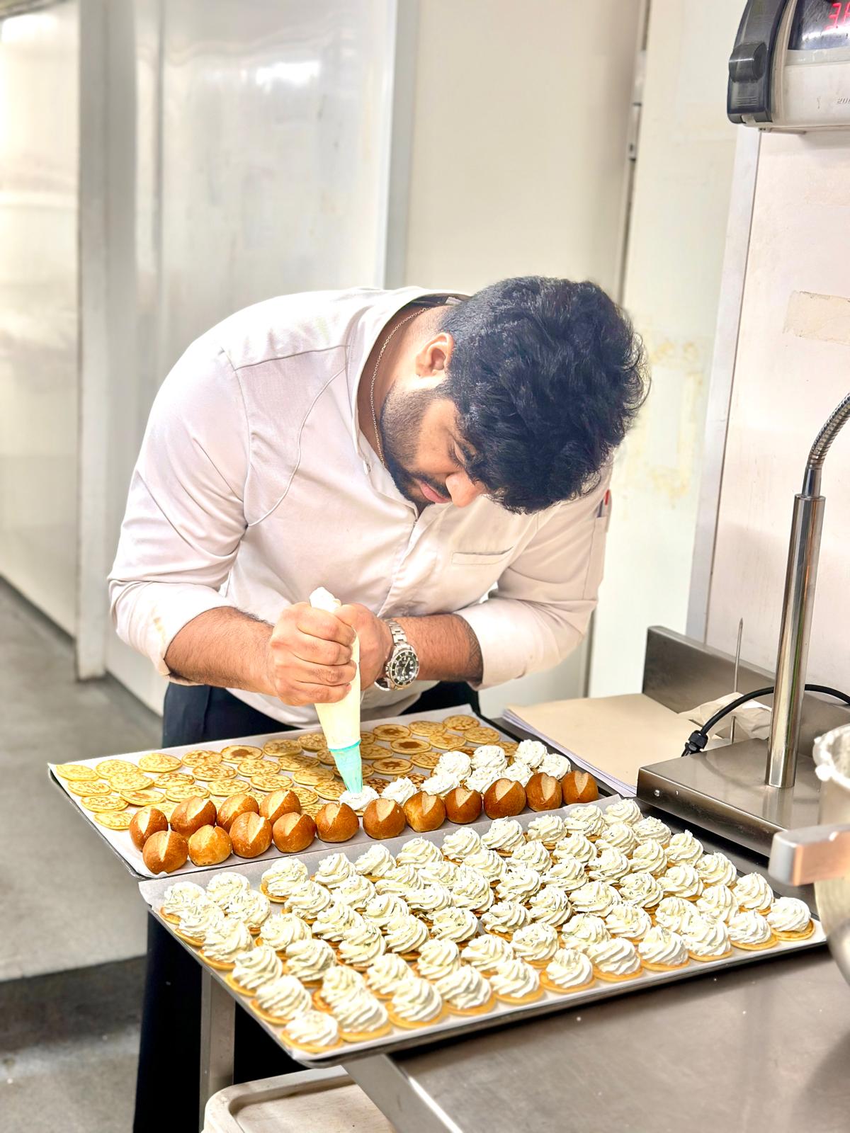 Chef Venu piping cream onto pastries in a professional kitchen